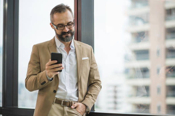istock Young handsome business bearded man standing post near window using smartphone in office work place. 1267471708