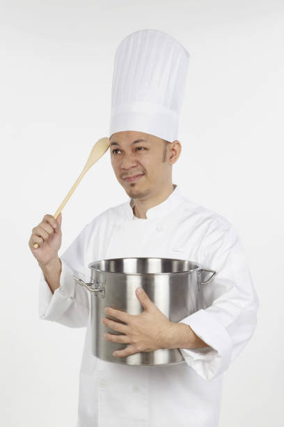 istock Asian chef holding a stew pot and a wooden spoon,looking stressed 1267473317