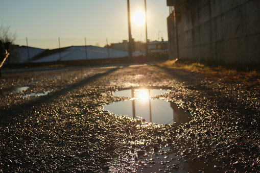 Pool of water in a country road with light reflected by the setting sun