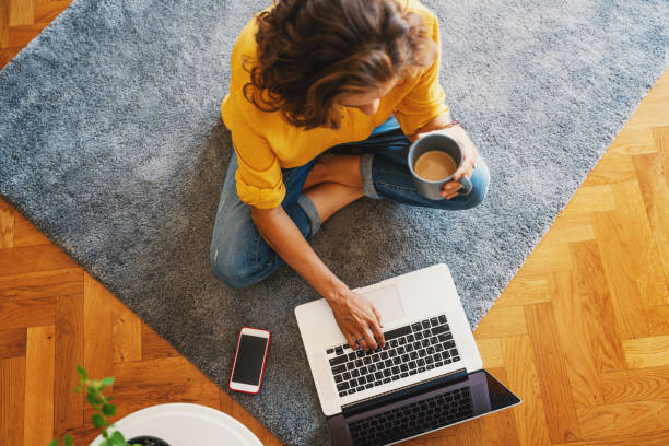 młoda dziewczyna w żółtej koszuli pracuje na laptopie z kubkiem kawy w domu w salonie na dywanie, pracy zdalnej i edukacji. widok z góry - photography carpet floor high angle view zdjęcia i obrazy z banku zdjęć