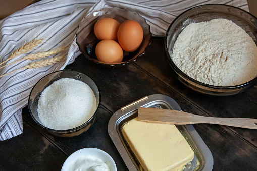 Baking ingredients for shortcrust pastry: butter, flour, eggs, sour cream, a towel on a wooden background. Flatley top view.