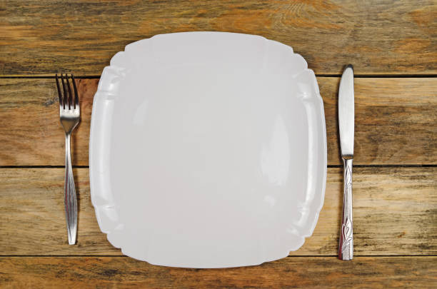 istock Empty white plate, knife, fork on a wooden background, top view, copy space 1267478153
