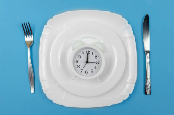 white alarm clock is on a white round plate which is in a larger white plate with a knife on