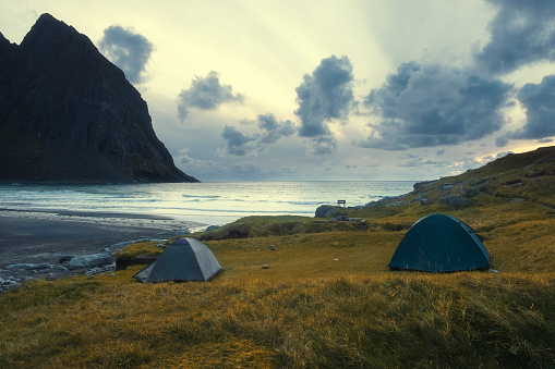 tourist tent on evening beach of Kvalvika in Norway, Lofoten islands mountains and sea background