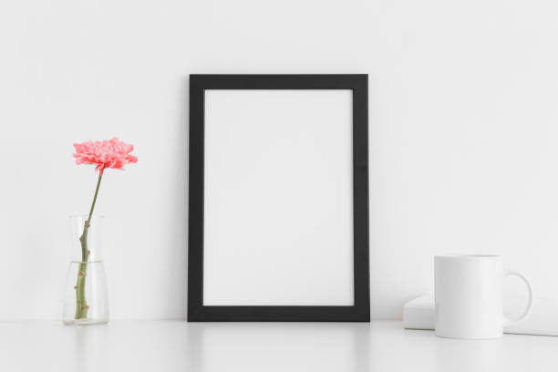 istock Black frame mockup with a chrysanthemum in a vase, book and a mug on a white table. Portrait orientation. 1267490016