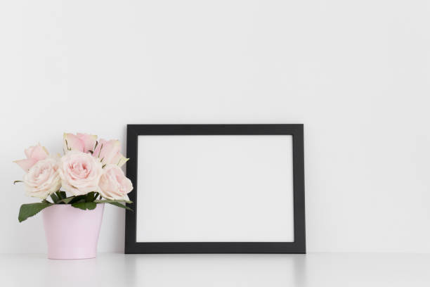 istock Black frame mockup with pink roses in a pot on a white table.Landscape orientation. 1267490074