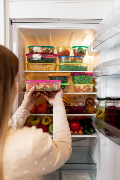 Woman taking raw food from refrigerator Close up shot of woman taking container with frozen mixed vegetables from refrigerator while looking at camera. happy green peas stock pictures, royalty-free photos & images