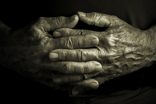 Elder senior adult with crossed wrinkled hands in a resting and relaxing position - black background