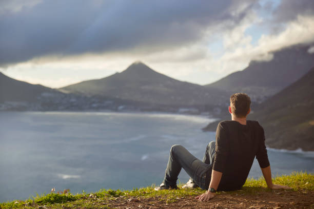 istock Young man contemplating view from top cliff 1267492392