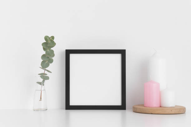 istock Black square frame mockup with candles and eucalyptus in a vase on a white table. 1267493511