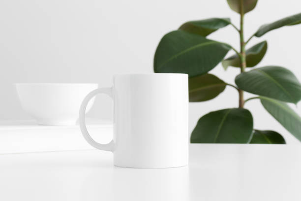 istock White mug mockup with workspace accessories on a white table and a ficus plant. 1267493877