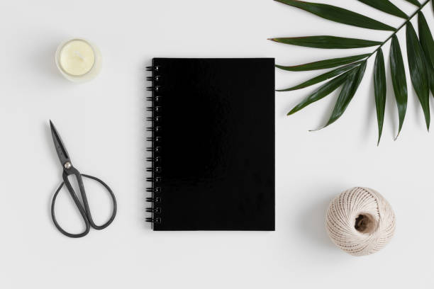 istock Top view of a black notebook mockup with  workspace accessories and a palm leaf on a white table. 1267494368