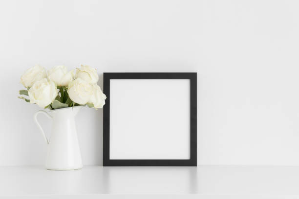 istock Black square frame mockup with a bouquet of white roses in a vase on a white table. 1267494608