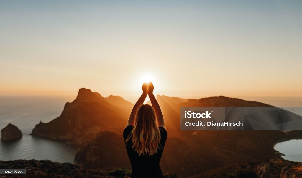 Young woman in spiritual pose holding the light Young woman in spiritual pose holding the light in front of mountains Nature Stock Photo