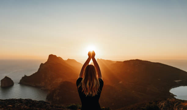 Young woman in spiritual pose holding the light Young woman in spiritual pose holding the light in front of mountains feelings stock pictures, royalty-free photos & images