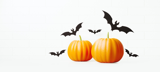 Pumpkins and flying bats over white brick wall background. Horizontal composition with copy space. Halloween concept.