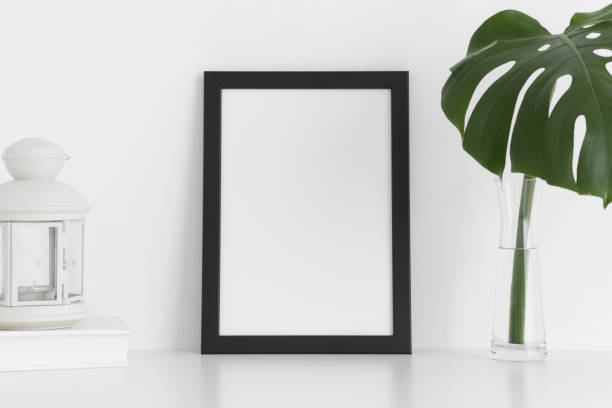 istock Black frame mockup with workspace accessories and a monstera leaf in a vase on a white table.Portrait orientation. 1267498758
