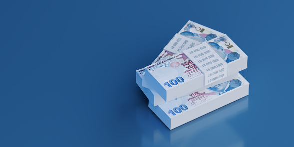 One hundred Turkish Lira stacks sitting on blue background. Selective focus. Horizontal composition with copy space. Stock market and finance concept.