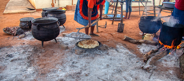Outdoors kitchen in an African village frying bread called dipapata  on the lid of a large cast iron pot