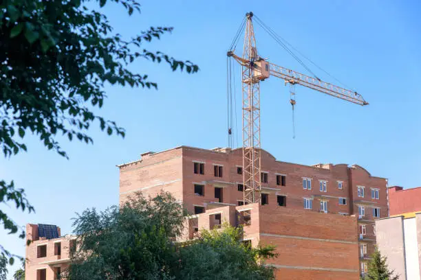 modern apartment building during construction with tower crane on blue sky background