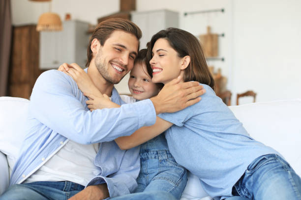 istock Positive friendly young parents with smiling little daughter sitting on sofa together while relaxing at home on weekend. 1267503247
