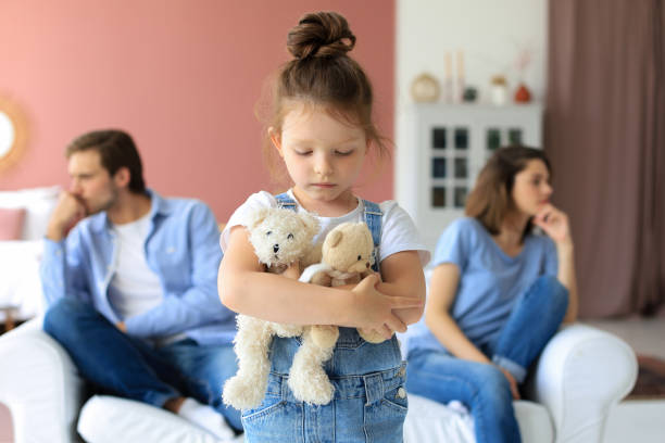 istock Young scolded parents sitting opposite each other on couch while little defenseless daughter upset looking at camera. 1267504858