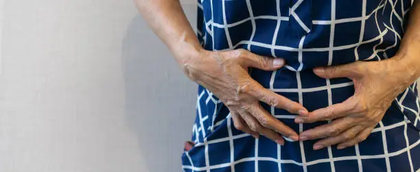 Photo of close up senior woman using hand to touching on stomach after feeling pain symptom at home for medical treatment and human body concept