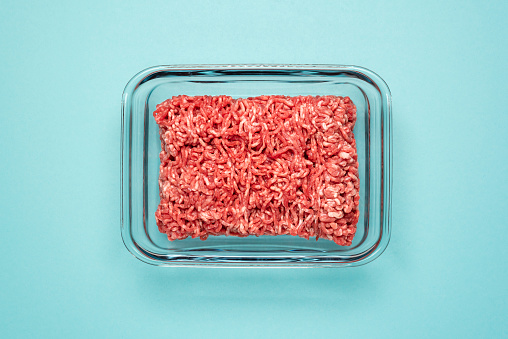 Above view with ground beef in a glass food container on a blue colored table. Ground beef in a glass dish isolated on a blue background.