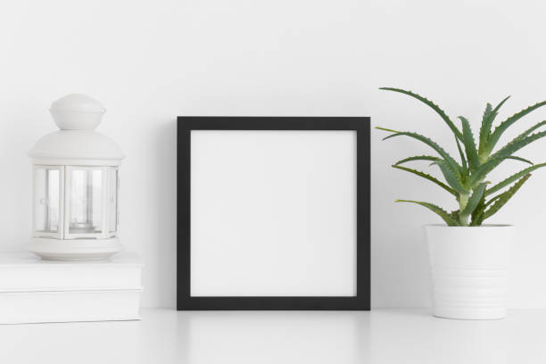 istock Black square frame mockup with a aloe vera in a pot, candle holder and a book on a white table. 1267509512
