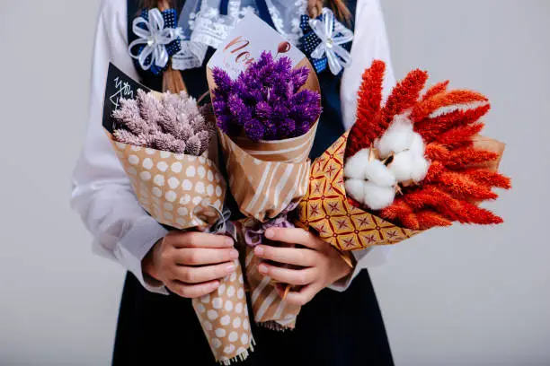 A three small bouquet with Phalaris and Amaranthus and cotton bolls , packed in craft paper in the hands of a girl with pigtails on a light background
