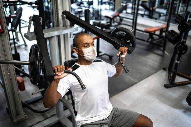 hombre haciendo ejercicio de entrenamiento de fuerza en el gimnasio con máscara facial - aparatos para hacer ejercicio fotos fotografías e imágenes de stock