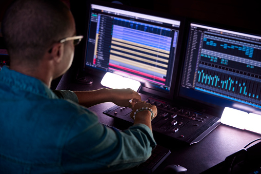 African-american producer working on music track on sound mixer control panel in music studio