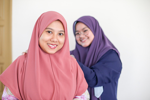 A Muslim female adult is helping her friend fitting 'tudung' (hijab).