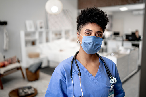 Retrato de una enfermera/médico joven en una llamada a casa con máscara facial photo
