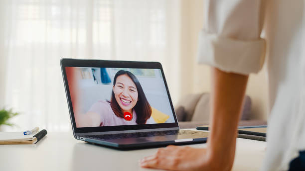 istock Young Asian business female using laptop video call talking with friends while working from home at living room. 1267516051