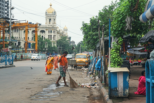 Esplanade, Kolkata, 07/12/2020: A municipal corporation worker cleaning roadside garbage with broom, but without wearing any face mask or gloves. Few woman are seen walking on street, wearing mask.
