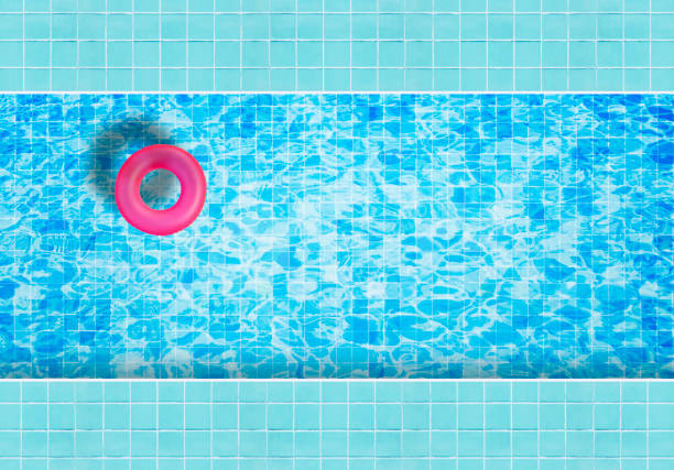 Pink inflatable floating ring floating on blue water in swimming pool surrounded with tiles mosaic floor from top view.