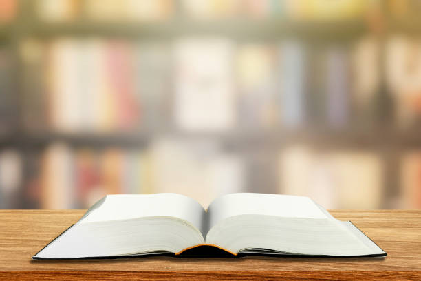 istock Opened book with blank page on wooden table with blurry image of library in background. 1267517589
