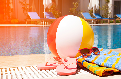 Beach ball, towel, sunglasses and flip-flops beside the swimming pool.