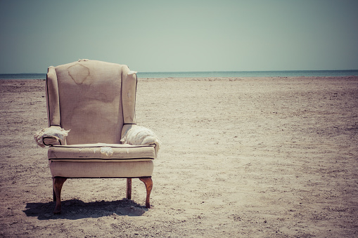 Eerie, creepy,  abandoned Arm Chair on the beach with blue skies