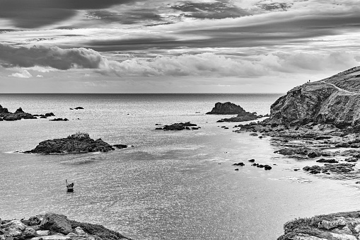 Rocky foreshore near Mousehole, Cornwall.  There is a fishing boat moored in the bay.