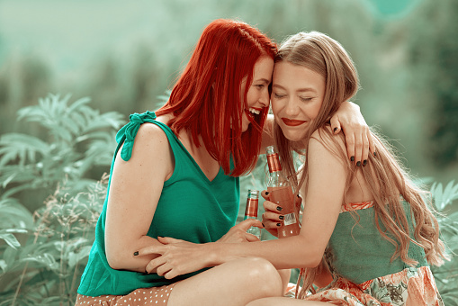 Redhead and blond girl at outdoors party drinking and holding bottles feeling happy