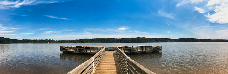 A serene lakeshore scene with a wooden dock, greenery, a boat, flowers, and a forest backdrop. Tranquil and dreamlike.A serene lakeshore scene with a wooden dock, greenery, a boat, flowers, and a forest backdrop. Tranquil and dreamlike.