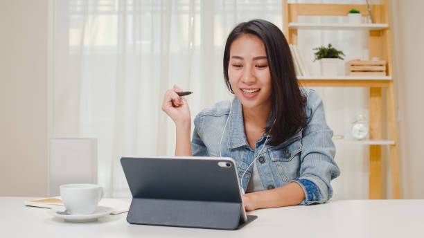 Freelance business women casual wear using tablet working call video conference with customer in workplace in living room at home. Freelance business women casual wear using tablet working call video conference with customer in workplace in living room at home. Happy young Asian girl relax sitting on desk do job in internet. asian adult student stock pictures, royalty-free photos & images