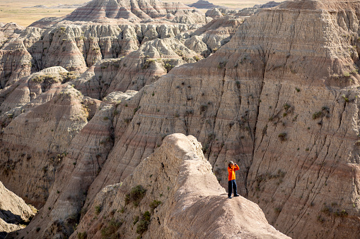 Male hiker looking with binoculars enjoying the landscape of the Badlands National Park while standing on a trail.