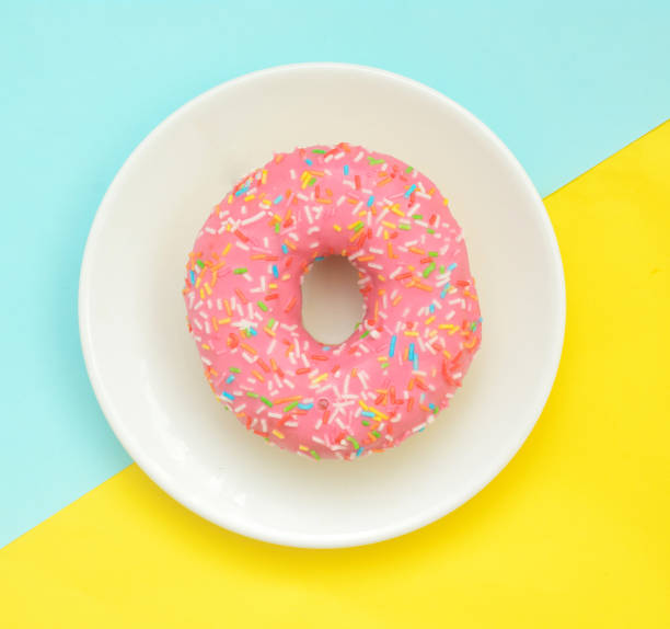 istock Pink glazes donut on white plate on pastel yellow turquoise background 1267561407