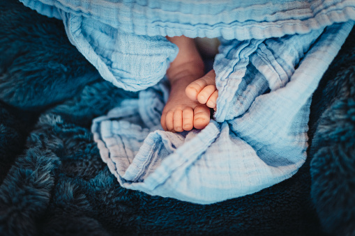 Adorable little baby feet peek out from under a blue blanket