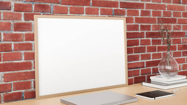 istock Horizontal poster frame mockup on the wooden table of home studio workspace with red brick wall. Side view, clipping path around poster picture. 1267563604