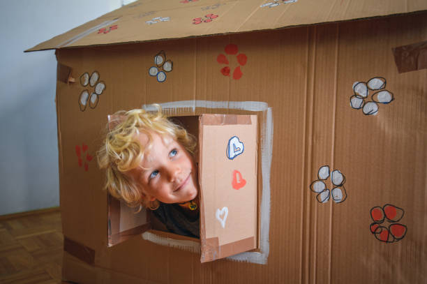 Caucasian boy looking through window of cardboard house Caucasian boy looking through window of cardboard house. He is happy and smiling. playhouse stock pictures, royalty-free photos & images