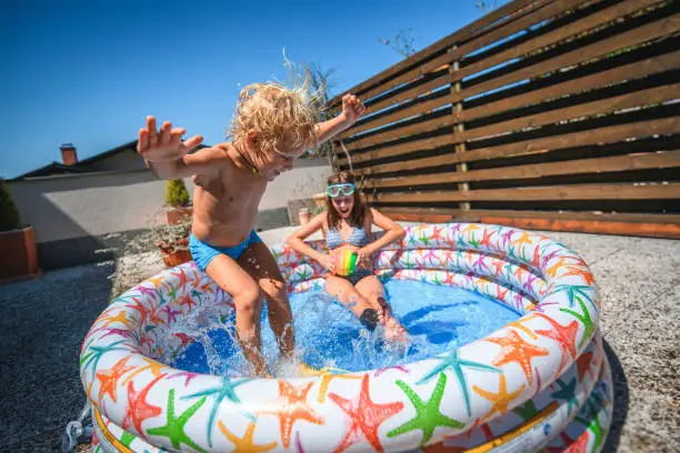 Photo of Cute Caucasian Brother and Sister Having Fun in Inflatable Swimming Pool at Home
